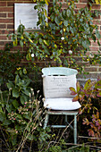 Stuhl und Kunstwerk im Blumenbeet an einer Backsteinmauer in St Lawrence, Isle of Wight, UK