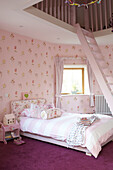 Einzelbett mit rosa Blümchentapete und Leiter zum Zwischengeschoss in einem Haus in Kent, England, UK