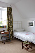 Einzelbett mit Schreibtisch und Stuhl am Fenster mit Vorhängen im Retrostil in einem Haus in Bembridge, Isle of Wight, Vereinigtes Königreich