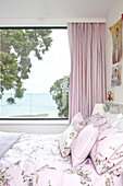 Rosa Vorhänge am Fenster mit geblümter Bettdecke im Schlafzimmer eines Hauses auf der Isle of Wight, England