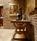 Tisch mit Töpfen und Skulpturen im Esszimmer mit freiliegender Backsteinwand und modernem Porträtgemälde