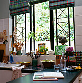 Close up of kitchen window with colourful checked roman blinds and worktop with kitchen clutter