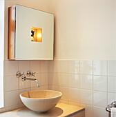 Corner detail of round stone wash hand basin and mirrored cabinet with integral lighting