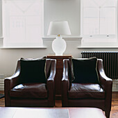 Two leather armchairs with velvet cushions and white table lamp close to windows