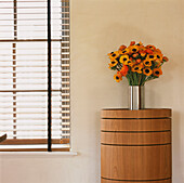 Window with venetian blinds and metallic vase with orange Anemone flowers