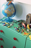 Close up of plastic toys and globe on green chest of drawers with red plastic handles 