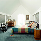 Weißes Dachgeschoss-Schlafzimmer unter der schrägen Traufe mit Schlagzeug-Truhe und Doppelbett