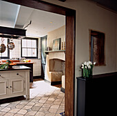 View from corridor of traditional kitchen in London town house with free standing furniture and stone fireplace