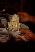 Chinese man serving freshly cooked noodles into a bowl in a street market in Shanghai China