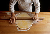 Person rolling out dough with a rolling pin on a floured wooden worktop in a kitchen
