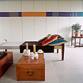 Monodruck auf einer Schrankwand hinter einem modernen Tagesbett und lackierten Truhen mit Blanc de Chine-Figuren