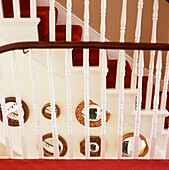 Hall stairs and landing with white painted banisters and red stair carpet with ornate circular wall mirrors 