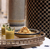 Schale mit gewürztem Couscous auf einem Tablett mit zwei Gläsern Minztee in einem marokkanischen Riad
