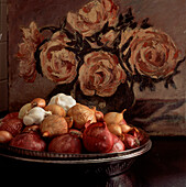 Still life with bowl of onions and garlic on tabletop with a floral oil painting in background
