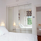 Blick auf ein weißes Schlafzimmer, das sich in verspiegelten Schranktüren spiegelt