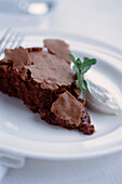 Schokoladenkuchen mit Mandeln und Armagnac, serviert mit Sahne und Minze auf einem weißen Teller