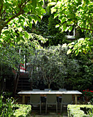 Üppiger grüner Garten mit Terrasse und großem Tisch und Stühlen