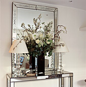 White flowers in a black glass vase in front of large Venetian mirror on Albrizzi mirrored console and glass table lamps