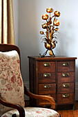 Ornate light on antique wooden drawers with armchair in London townhouse, UK