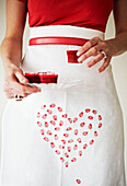 Low section woman in heart shaped apron holding red cupcakes