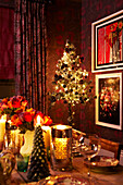 Colourful christmas table setting in red and gold with roses and candlelight and christmas tree