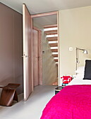 Bright pink bed cover with wooden stool and view through doorway in contemporary London home, England, UK