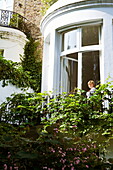 Woman stands in curved bay window of London townhouse, England, UK