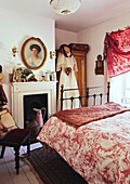 White dress hangs on wardrobe at fireside in bedroom with red patterned duvet in Evershot home, Dorset, Kent, UK
