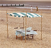 Tisch und Stühle am Strand unter einem gestreiften Baldachin
