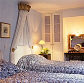 Zwillingsbetten mit Baldachin und beleuchteten Lampen in einem pastellblauen Schlafzimmer