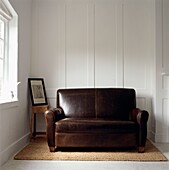 Brown leather two-seater sofa on seagrass rug with white panelled wall