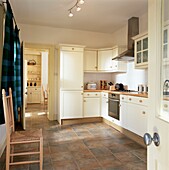 Blick durch eine offene Tür in einer gefliesten Landhausküche mit weißen Einbaumöbeln