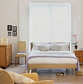 Double bed in front of sunlit window with closed blinds in room with and light wood furniture 