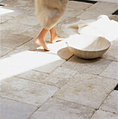 Low section of woman walking across stone floor with wash bowl