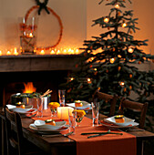 Christmas table setting in orange colours with open fire and twinkling candles