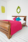 Schlittenbett aus Holz in einem ganz in Weiß gehaltenen Schlafzimmer mit farbenfroher rosa Tagesdecke und Kissen sowie einem verzierten, bemalten Spiegel