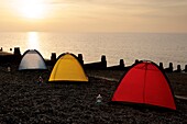 3 bunte Zelte in einer Reihe am Strand von Whitstable, beleuchtet von der untergehenden Sonne, mit brennenden Kerzen unter Gläsern