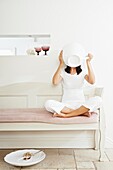 Woman sitting cross-legged on bench seat drinking from oversized teacup