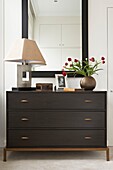 Lamp and cut tulips on dark wood chest of drawers below mirror in London home