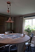Wooden circular dining table with metal chairs under brass pendant light Kingston home,  East Sussex,  England,  UK