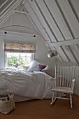 Weiß gestrichener Schaukelstuhl und ungemachtes Bett im Schlafzimmer im Dachgeschoss des Hauses in Kingston, East Sussex, England, UK
