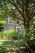 Vogelfutterspender und Metallbank unter einem Baum im Garten eines Hauses in Kent, England UK
