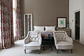 Pair of buttoned armchairs with long curtains in bedroom of South Kensington townhouse  London  UK