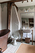 Waschbecken und Bidet mit Pantoffelbadewanne und freigelegtem, gekalktem Mauerwerk in einem Haus in Suffolk, England, UK