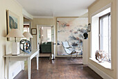 Pair of cream lamps on table with large art canvas and chair in hallway of Suffolk farmhouse  England  UK