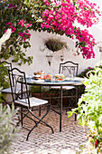 Rosa Bougainvillea über schmiedeeisernem Tisch und Stühlen im Innenhof von Castro Marim, Portugal