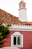 Gefliestes Dach und Schornstein mit Fenster in roten Mauern eines Hauses in Castro Marim, Portugal