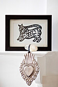 Framed artwork of cat and silver heart shaped ornament on mantlepiece in Brighton home East Sussex England UK