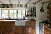 Belfast sink with crockery on wooden shelving at window in Devon kitchen England UK