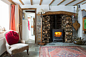 Befeuerter Holzofen und gestapeltes Brennholz in einem Cottage in Devon, England, UK